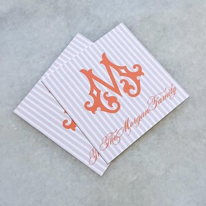 Op de afbeelding: Twee vierkante papieren servetten met een gestreept patroon in wit en lichtroze. Elke servet heeft een oranje, sierlijke letter "M" en de tekst "The Morgan Family" in bijpassend oranje schrift.