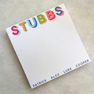 Op de afbeelding: Witte notitieblok met de naam "STUBBS" in kleurrijke 3D-letters bovenaan. De namen "PATRICK", "ALEX", "LUKE" en "COOPER" zijn in blauw gedrukt, voor een persoonlijk tintje.