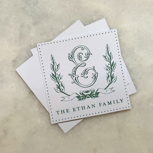 Op de afbeelding: Een witte kaart met een groen-wit ontwerp. De kaart heeft een gestileerde letter "E" met een krans van bladeren en een lint met de tekst "The Ethan Family".