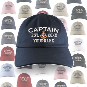 May include: A collection of navy blue, beige, pink, red, and gray baseball caps with different nautical themed embroidery. The caps feature the words "Captain", "First Mate", "Skipper", "Crew", and "Deckhand" with an anchor and the year 20XX. The text "Your Name" is also included on each cap.
