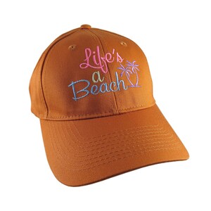 May include: A brown baseball cap with the embroidered phrase "Life's a Beach" in pink, blue, and green. The cap has a curved peak and a classic six-panel design, ideal for sun protection.