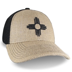 May include: A beige and black trucker hat with a black embroidered Zia symbol on the front. The hat has a mesh back.