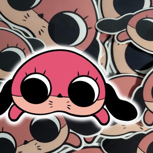 May include: A pink cartoon dog sticker with large black eyes and a white outline. The dog has floppy ears and a small black nose.