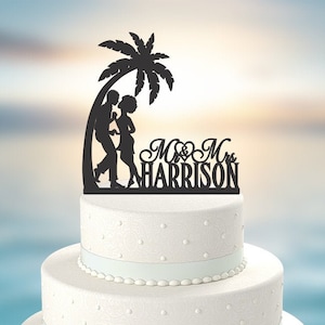 May include: Black silhouette cake topper of a couple standing under a palm tree with the text "Mr. & Mrs. HARRISON" below.