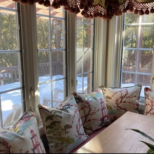 Pode incluir: Uma janela de ba&iacute;a com vista para um jardim nevado. A janela &eacute; decorada com uma cornija com borlas. Uma mesa de madeira com um conjunto de almofadas com padr&atilde;o floral fica em frente &agrave; janela.