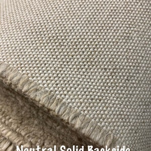 Pode incluir: Close-up de um tecido bege com textura tecida. O tecido tem uma borda desfiada e as palavras "Neutral Solid Backside" est&atilde;o impressas na parte inferior da imagem.