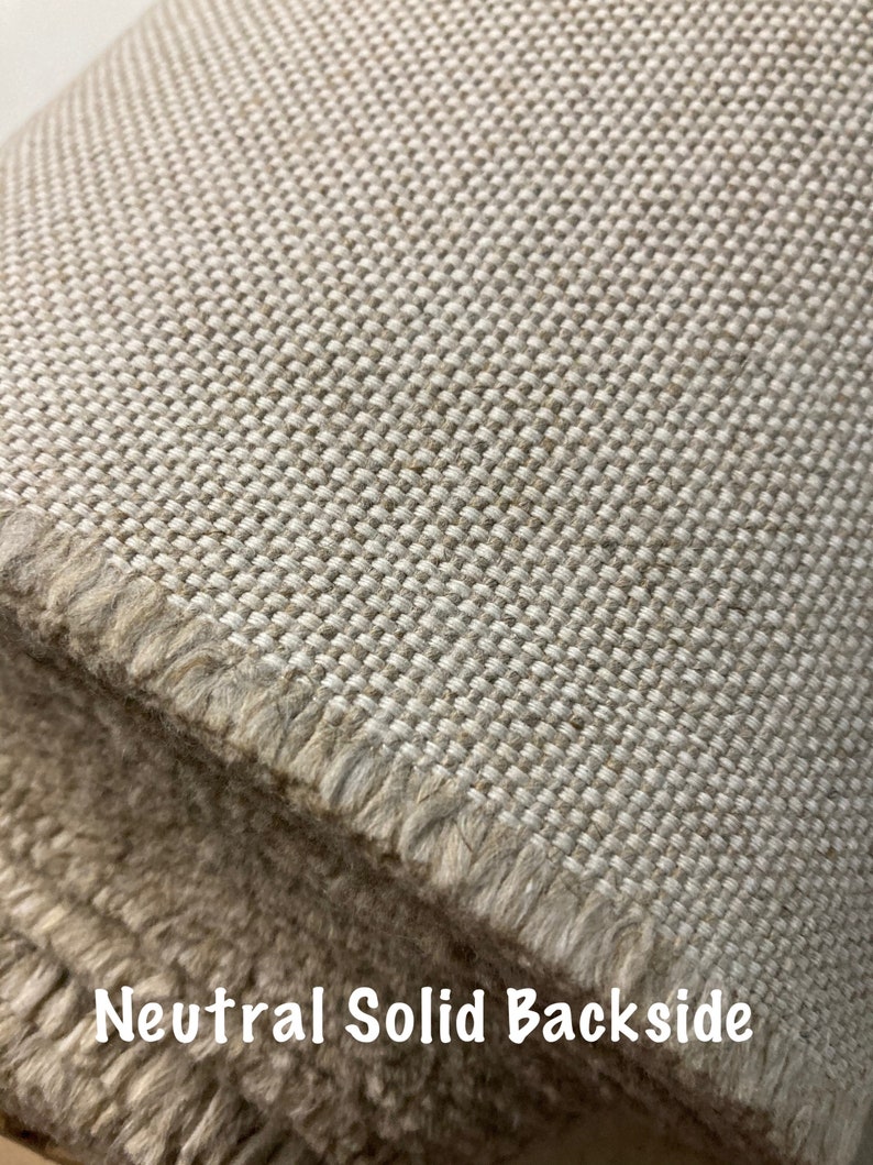 Pode incluir: Close-up de um tecido bege com textura tecida. O tecido tem uma borda desfiada e as palavras "Neutral Solid Backside" est&atilde;o impressas na parte inferior da imagem.