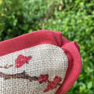 Pode incluir: Close-up de um travesseiro vermelho e bege com um padr&atilde;o floral. O travesseiro tem uma borda vermelha e uma textura tecida.