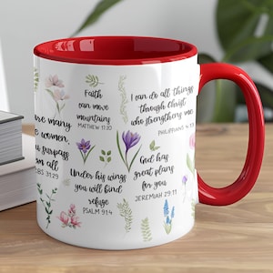 May include: White ceramic mug with a red interior and handle. The mug is decorated with floral illustrations and inspirational quotes from the Bible. The text includes phrases like "Faith can move mountains" and "I can do all things through Christ."