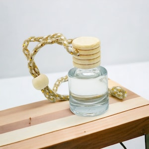 May include: A clear glass bottle with a wooden lid and a beige and gold string attached. The bottle is sitting on a wooden surface.