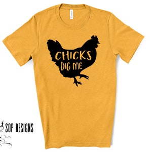 May include: Mustard yellow t-shirt with a black silhouette of a chicken and the text "CHICKS DIG ME". The shirt has short sleeves and a crew neck. The brand "SOP DESIGNS" is printed in black on the bottom left.