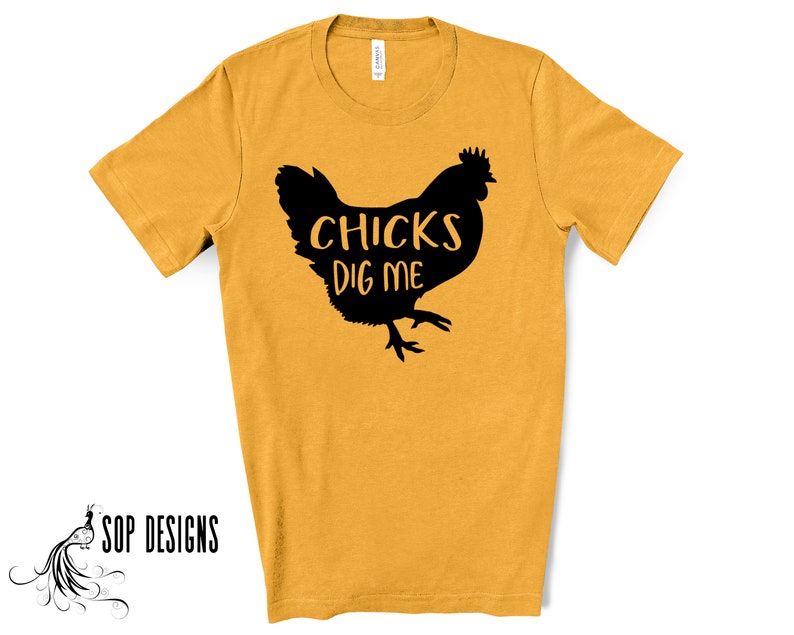 May include: Mustard yellow t-shirt with a black silhouette of a chicken and the text "CHICKS DIG ME". The shirt has short sleeves and a crew neck. The brand "SOP DESIGNS" is printed in black on the bottom left.