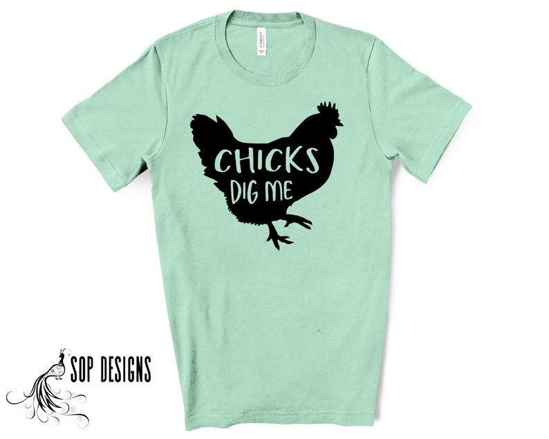May include: A light green t-shirt with a black silhouette of a chicken and the words "CHICKS DIG ME" printed on the front. The shirt is made of a soft material and has short sleeves. The brand "SOP DESIGNS" is printed on the bottom left.