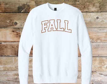 Puede incluir: Una sudadera blanca con la palabra "FALL" en marrón, con una fuente de estilo universitario. La parte superior de manga larga está hecha de un material suave y es adecuada para climas más fríos. La sudadera se muestra sobre un fondo de madera.