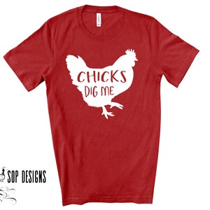 May include: Red t-shirt with a white graphic of a chicken and the text "CHICKS DIG ME". The shirt is a short-sleeved crew neck. The brand "SOP DESIGNS" is printed in black at the bottom left.