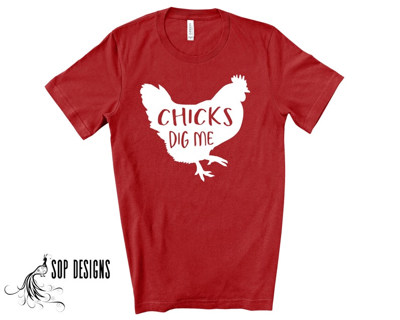 May include: Red t-shirt with a white graphic of a chicken and the text "CHICKS DIG ME". The shirt is a short-sleeved crew neck. The brand "SOP DESIGNS" is printed in black at the bottom left.