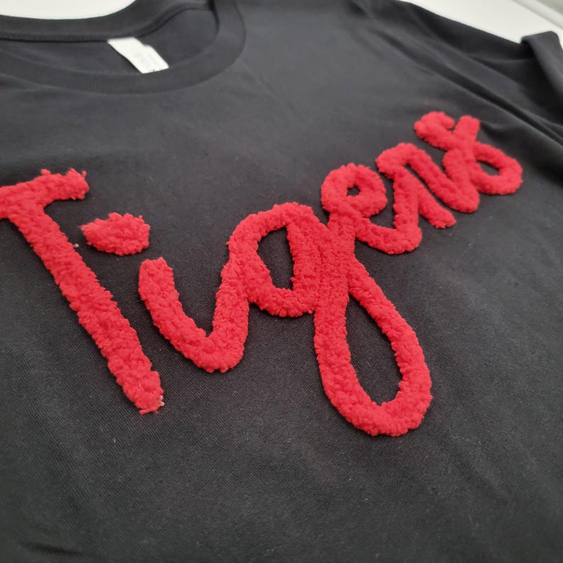 May include: Black t-shirt with a red, fuzzy, embroidered "Tigers" design.
