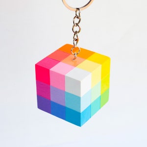 May include: A colorful wooden cube keychain with a rainbow pattern. Each side of the cube is a different color, creating a vibrant and playful design.