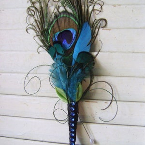 May include: A peacock feather boutonniere with blue and green feathers, a green ribbon, and a black base with blue rhinestones.