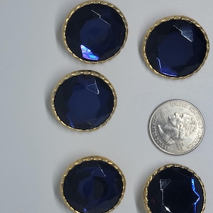May include: Five circular buttons featuring faceted dark blue centers set within gold-toned twisted metal rims. A United States quarter coin is positioned next to the buttons to provide a clear visual reference for their size and scale.
