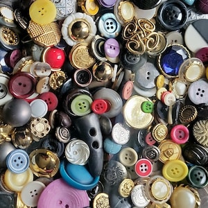 May include: A collection of various buttons in different sizes, shapes, and colors. The buttons include a variety of materials, such as plastic, metal, and fabric. Colors include red, yellow, blue, green, white, and gold. Some buttons have decorative designs.