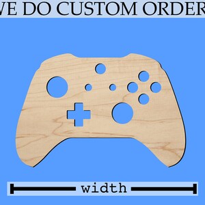 May include: A wooden cutout of a video game controller in the shape of an Xbox controller. The controller is light brown and has a blue background. The controller is approximately 7 inches wide.
