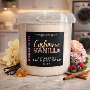 Może przedstawiać: Przezroczysty plastikowy pojemnik wypełniony proszkiem do prania. Etykieta głosi "Cashmere Vanilla" i "Oxy-Boosted Laundry Soap". Pojemnik otoczony jest kwiatami, laskami wanilii i laskami cynamonu. Produkt ma 907 gram&oacute;w.