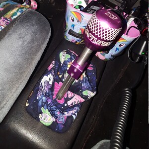 May include: A purple and silver car gear shift knob with a black and pink My Little Pony themed gear shift boot. The knob has a grid pattern and the text "K-TUNER" on it.