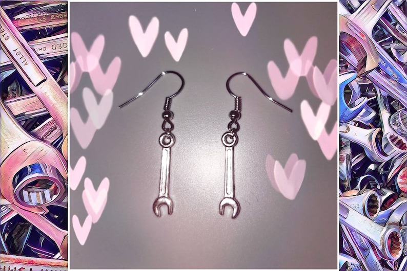 May include: Silver-colored wrench earrings with a hook closure. The earrings are in the shape of a wrench and are suspended from a silver hook. The background has a blurred effect with pink hearts and a collection of wrenches.
