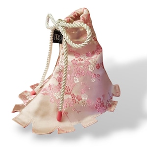 May include: A pink satin drawstring bag with a white cord and a pink floral pattern. The bag has a scalloped edge and a white cord with a pink tassel.
