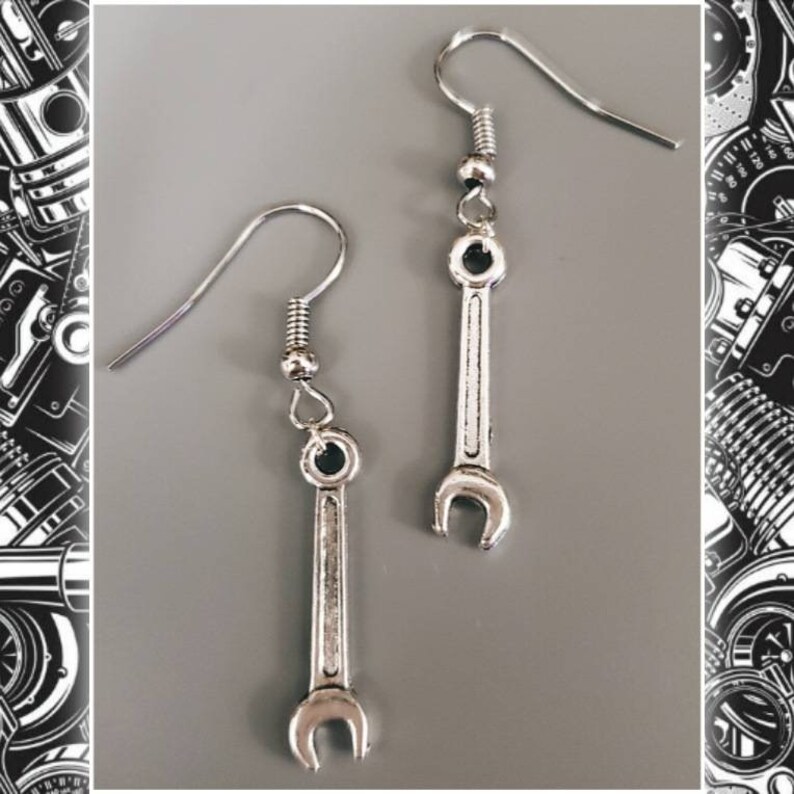 May include: A pair of silver-colored wrench earrings. Each earring features a small wrench charm suspended from a hook. The wrenches have a detailed, realistic design, with a small circular accent at the top and bottom.