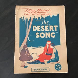 May include: Vintage souvenir booklet for "The Desert Song" operetta. The cover features illustrations of figures in desert attire, with the title in large blue letters. The booklet is tan with red and blue accents and the price is 25¢.