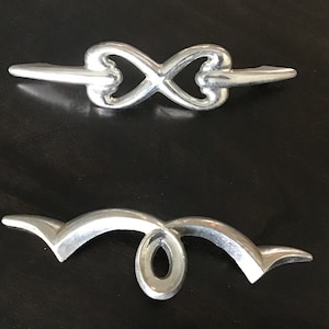 May include: Two silver metal drawer pulls. The top pull is shaped like an infinity symbol. The bottom pull is a curved shape with a loop in the center.