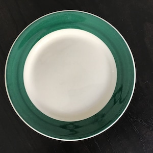 May include: A white ceramic plate with a green rim. The rim has a subtle swirl pattern.