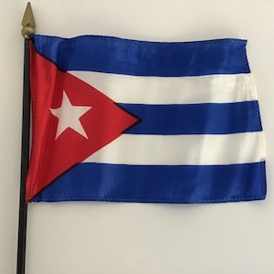 以下が含まれることがあります： 金色の槍の先端の付いた黒い棒に、小さなキューバの国旗が取り付けられています。旗は青色で、白い帯、赤い帯、白い帯があります。旗の左上には、白い星が描かれた赤い三角形があります。