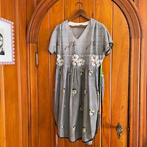 May include: A gray and white floral dress with a black and white striped bodice. The dress has a V-neck and short sleeves. It is hanging on a wooden hanger.