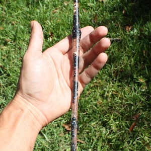 May include: A long, clear, cylindrical wand with a rounded tip. The wand is filled with small, black and silver beads.