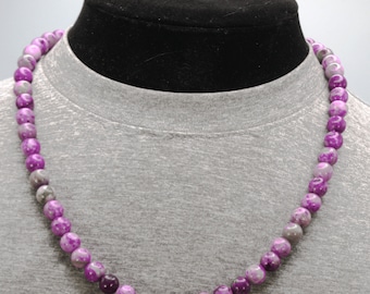 May include: A purple and gray beaded necklace with a mottled pattern. The necklace is made of round beads and is displayed on a gray mannequin.