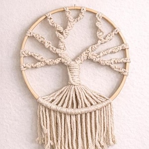 May include: A handmade macrame wall hanging featuring a tree design inside a 12 inch wooden hoop. The off-white cord is knotted to form branches and roots. Text reads: Handmade Macrame Wall Hanging, 12 Inch Wooden Hoop, Auras by Osiris, HANDCRAFTED MACRAME DECOR.