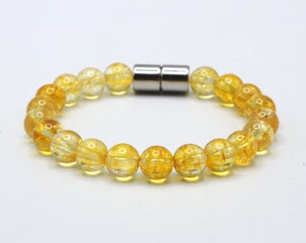 May include: A bracelet featuring golden-yellow, translucent beads with internal striations. The beads are strung together, connected by a silver-colored magnetic clasp. The bracelet is displayed on a white background.