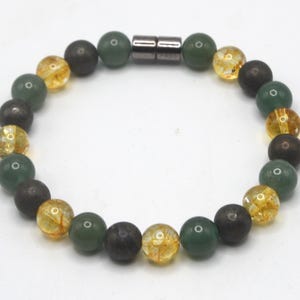 May include: A beaded bracelet featuring a mix of dark gray, green, and yellow-orange beads. The bracelet is held together by a magnetic clasp. The beads have a variety of textures, with some appearing smooth and others more textured.