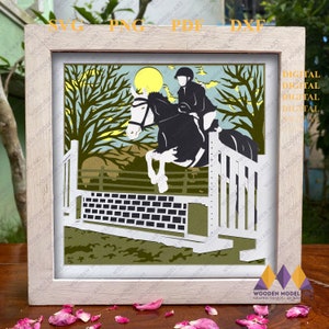 Puede incluir: Una obra de arte en papel recortado enmarcada que representa un caballo y un jinete saltando una valla. La obra presenta un caballo blanco y negro, un jinete con casco y un sol amarillo en un cielo azul. El marco es de color claro, con el texto "SVG PNG PDF DXX" y "DIGITAL".