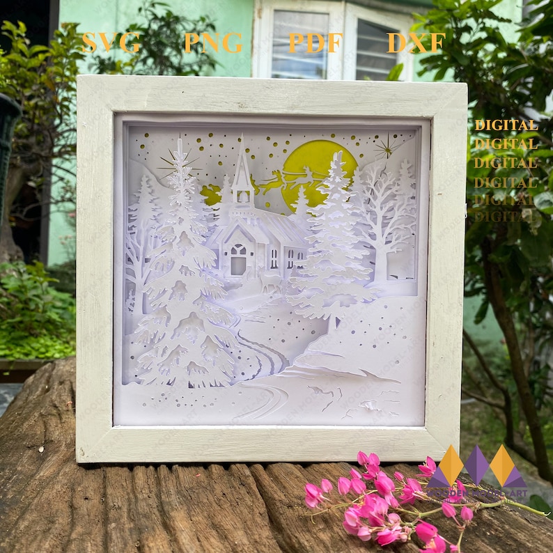 May include: A white papercut art piece in a white frame depicting a snowy winter scene with a church, trees, and a crescent moon. The scene is illuminated with a yellow glow. The words "DIGITAL DIGITAL DIGITAL DIGITAL DIGITAL" are visible on the right side of the image.