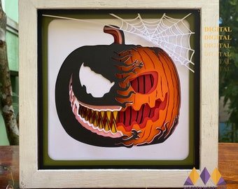 Puede incluir: Un modelo de papel 3D de una calabaza con una cara de Venom en un lado. La calabaza es naranja y roja, y la cara de Venom es negra con ojos y dientes blancos. El modelo está enmarcado en un marco blanco con un passe-partout verde.