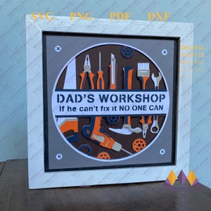 Op de afbeelding: Een wit ingelijst beeld met een grijze achtergrond en een cirkel in het midden. De cirkel heeft een bruine achtergrond met oranje en zwarte gereedschappen en tandwielen. De tekst "DAD'S WORKSHOP" en "If he can't fix it NO ONE CAN" is wit.