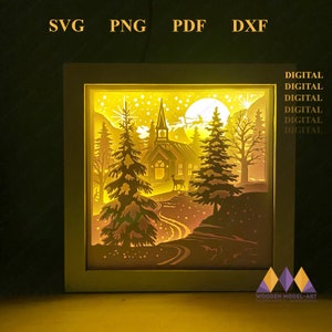 May include: A digital download of a 3D layered papercraft design for a lighted Christmas scene. The design features a church, trees, a path, and a deer in a snowy forest setting. The design is illuminated by a warm yellow light.