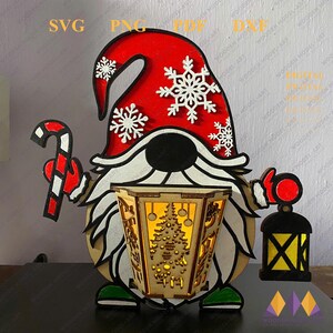 May include: A red and white gnome holding a candy cane and a lantern. The gnome has a white beard and a red hat with snowflakes. The lantern has a light inside and a Christmas tree design.