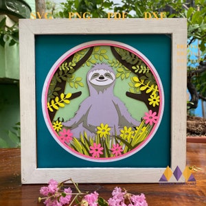 May include: A papercraft of a sloth meditating in a circle of green leaves and pink flowers. The sloth is purple and has a happy expression. The background is teal.