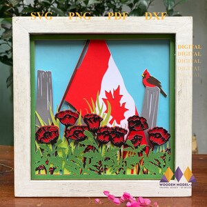 May include: A white frame with a red, white, and green paper craft inside. The craft depicts a Canadian flag, red poppies, and a cardinal bird. The text "DIGITAL" is repeated multiple times on the frame.