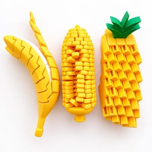 Op de afbeelding: Drie beweegbare plastic figuren in de vorm van fruit en groenten: een gele banaan met een witte kern, een gele maïskolf met een textuurrijk oppervlak en een gele ananas met een groene bladeren top, allemaal met een geometrisch blokontwerp.